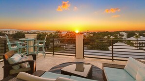 A rooftop terrace with outdoor furniture, a view of the sunset, and distant buildings. - Blue Mountain on 30A - Rooftop Views - Pool - Steps to Beach! (Santa Rosa Beach)