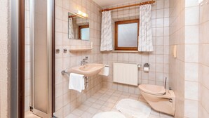 A bathroom with a glass shower enclosure, a sink with a mirror, a toilet, and a window with curtains. - Vacation apartment with balcony and mountain view, 42 sqm in a central location (Reit im Winkl)