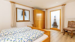 A bedroom with a bed, wooden wardrobe, chair, and a view through a window. - Vacation apartment with balcony and mountain view, 42 sqm in a central location (Reit im Winkl)