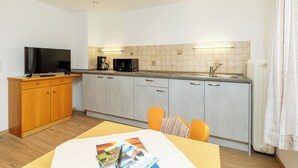A compact kitchen with a flat-screen TV, microwave, and coffee maker. There is a dining table with chairs and a magazine on it. - Vacation apartment with balcony and mountain view, 42 sqm in a central location (Reit im Winkl)