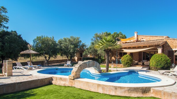 Una piscina con arco in pietra, circondata da un prato curato e lettini.