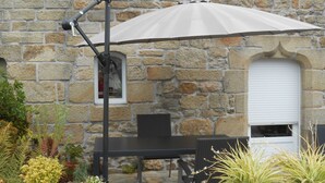 Een stenen gebouw met een patio, inclusief een tafel, stoelen, een hangende parasol en potplanten.