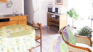 Een kleine keuken met houten kastjes, een magnetron en een eethoek met een tafel bedekt met een bloemenkleed.