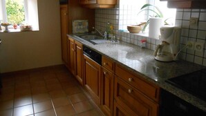 Een keuken met houten kastjes, een spoelbak, een fornuis en een raam met uitzicht op groen.