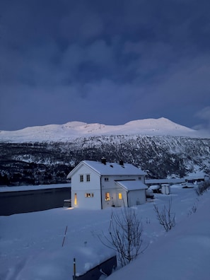 A snow-covered landscape with a house and a mountain in the background.