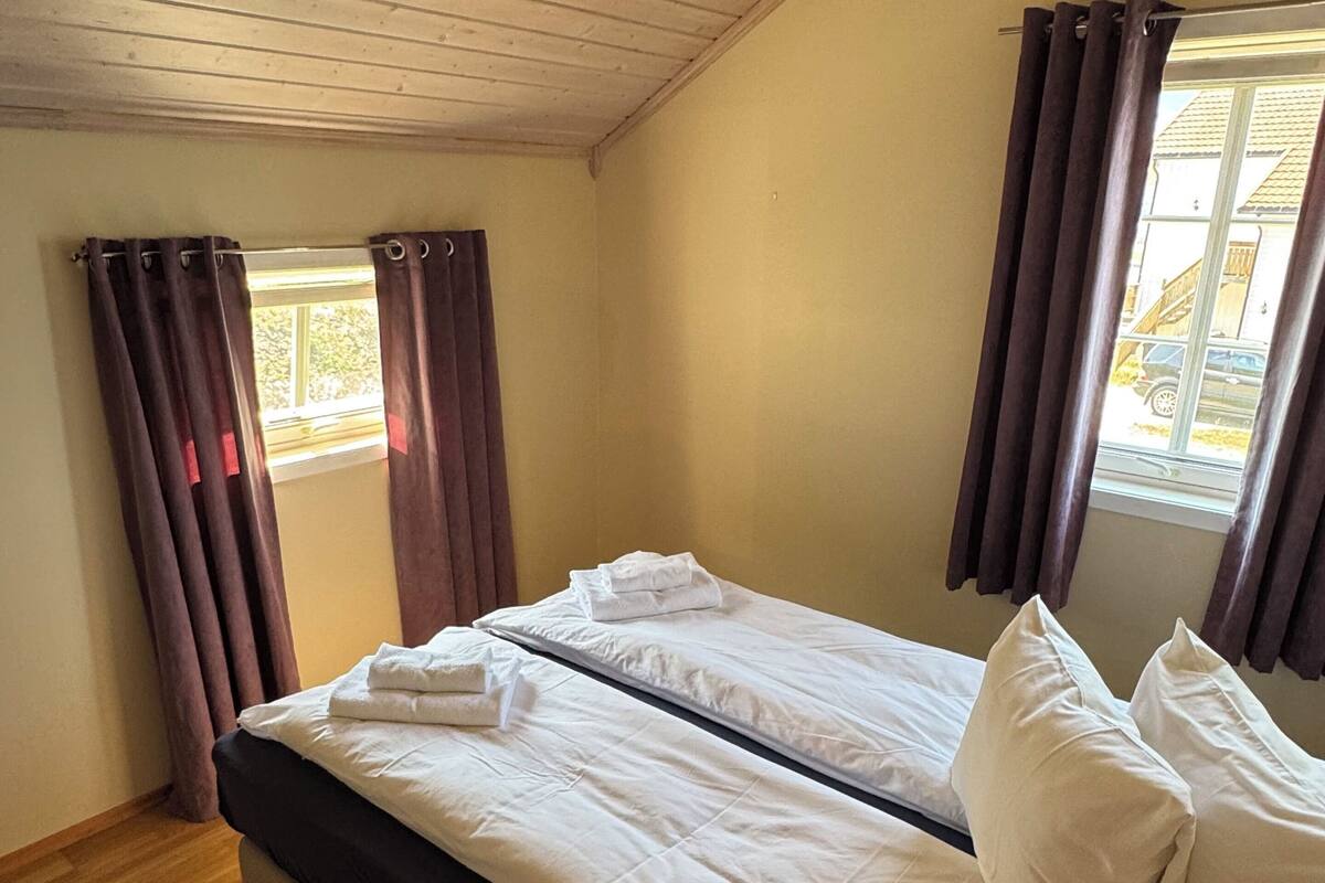 Ein Zimmer mit einem Bett, Holzboden und einem Fenster mit Vorhängen.