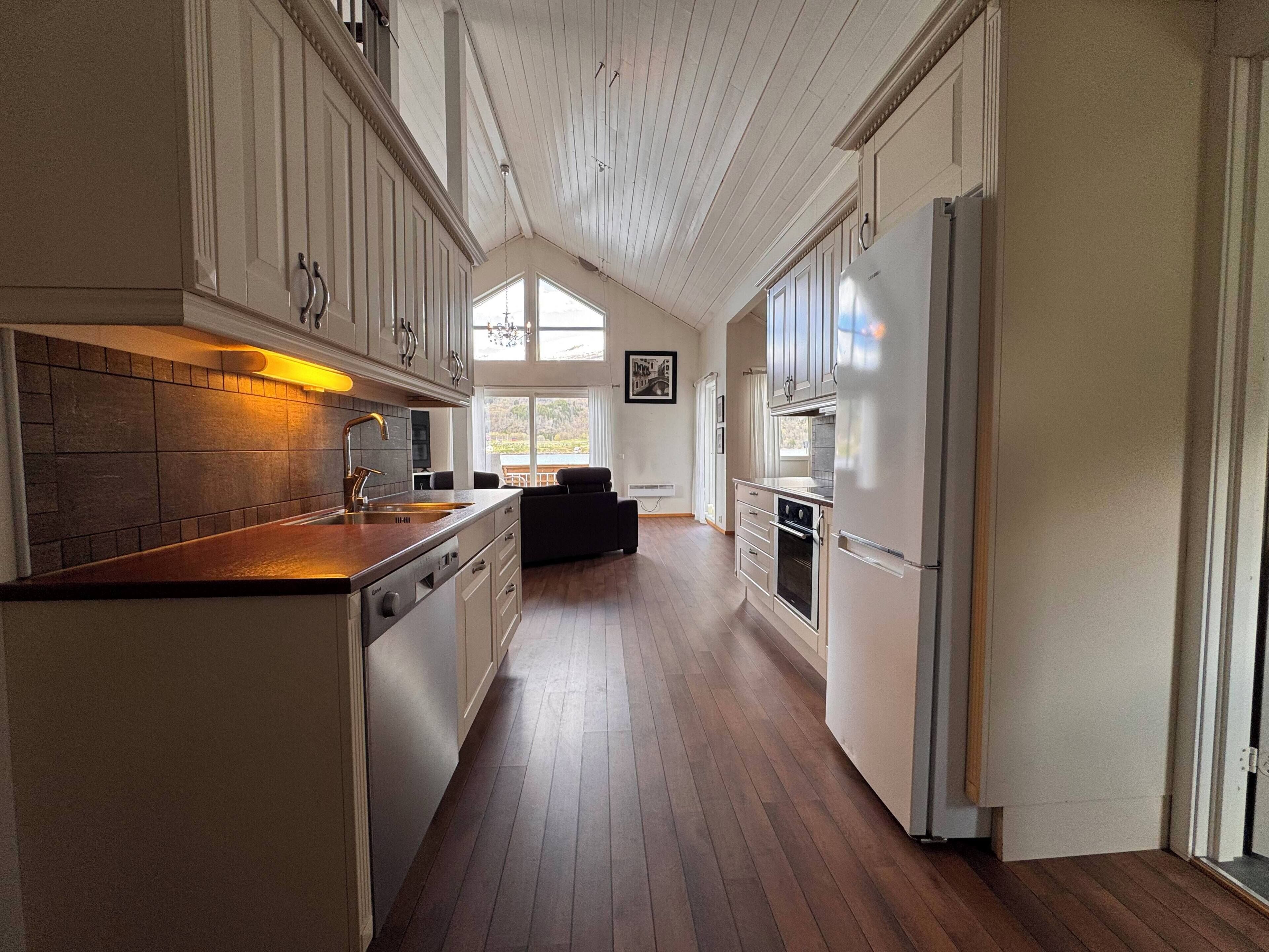 Une cuisine spacieuse dotée d’un plancher en bois, de meubles blancs et d’un grand îlot central avec un évier.