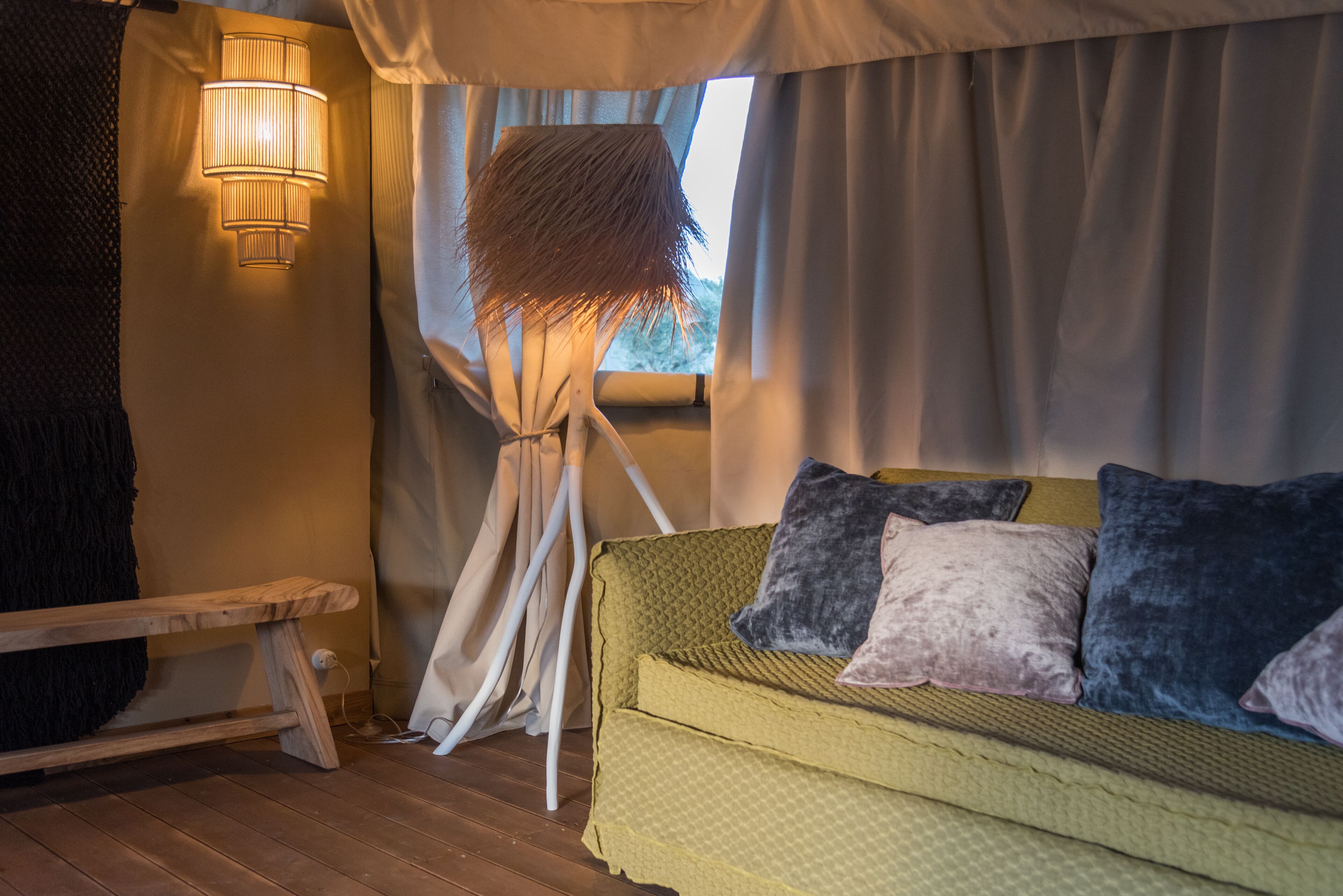 A cozy room with a green sofa, a bench, and a lamp with a textured shade.