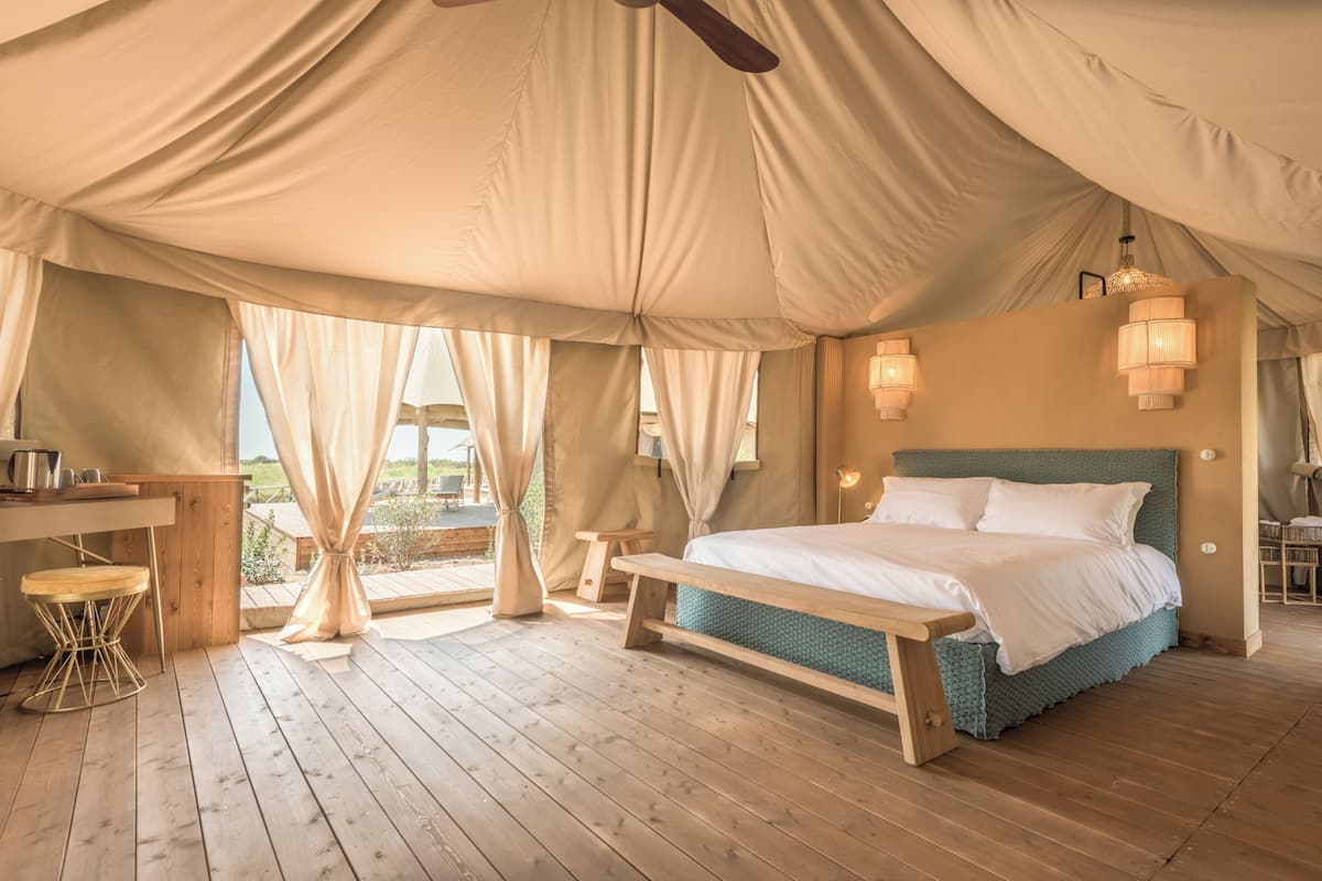 A tented room with a bed, wooden bench, and a table with chairs.