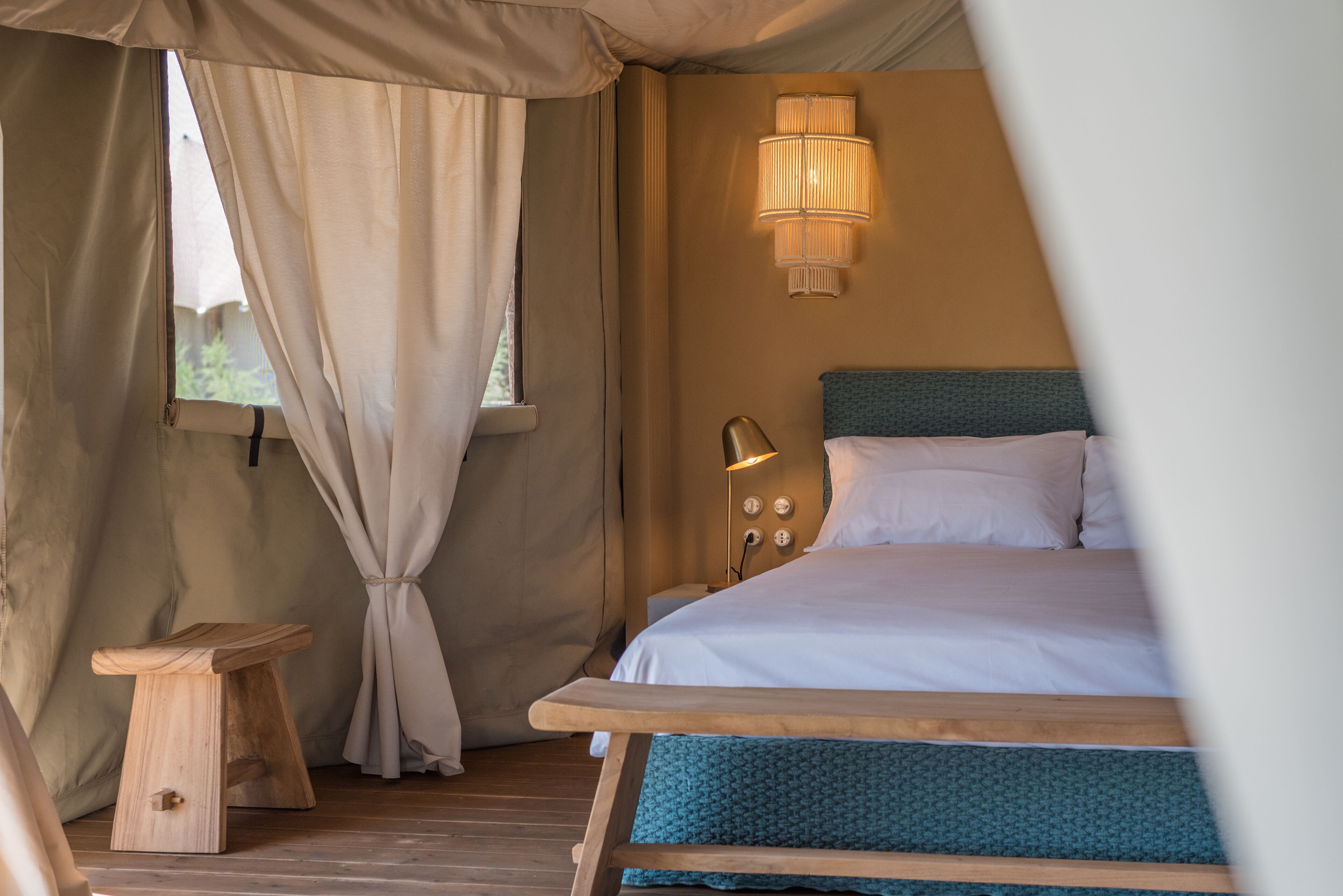 Una habitación con tienda de campaña, una cama, una mesita de noche y un taburete de madera.
