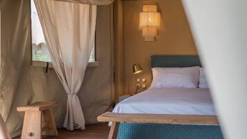 Una habitación con tienda de campaña, una cama, una mesita de noche y un taburete de madera.