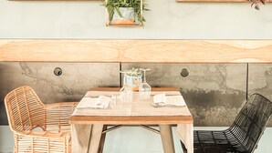 A dining area with a wooden table, two wicker chairs, and a wall-mounted plant shelf. - Terme di Vulci Glamping & SPA (Canino)