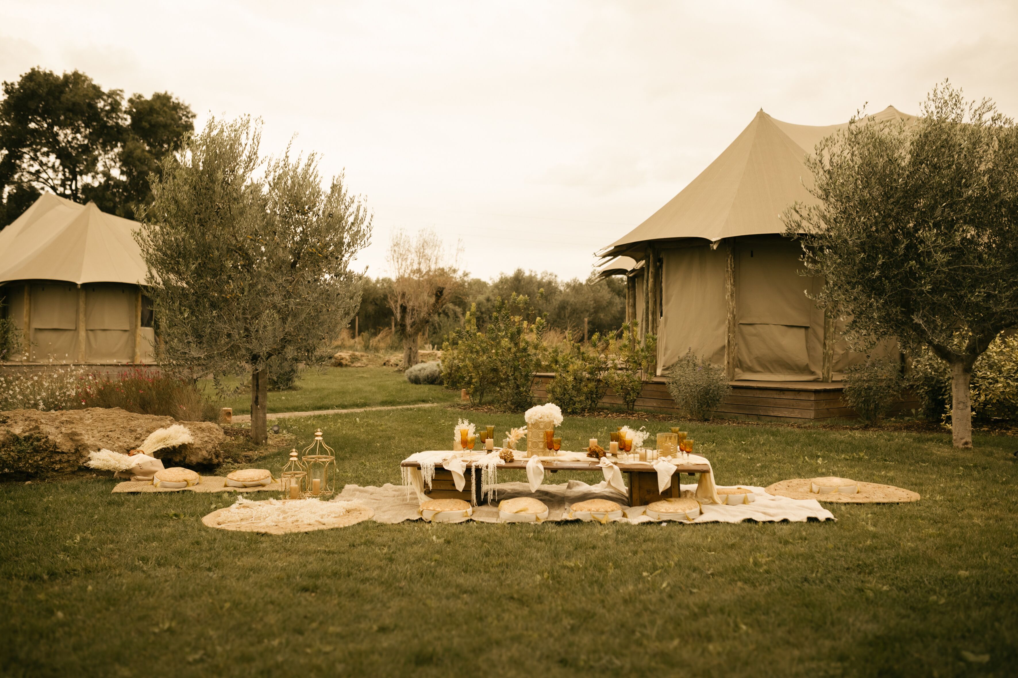 A tented outdoor dining area with tables set for a meal, surrounded by trees and greenery.