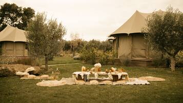 A tented outdoor dining area with tables set for a meal, surrounded by trees and greenery.