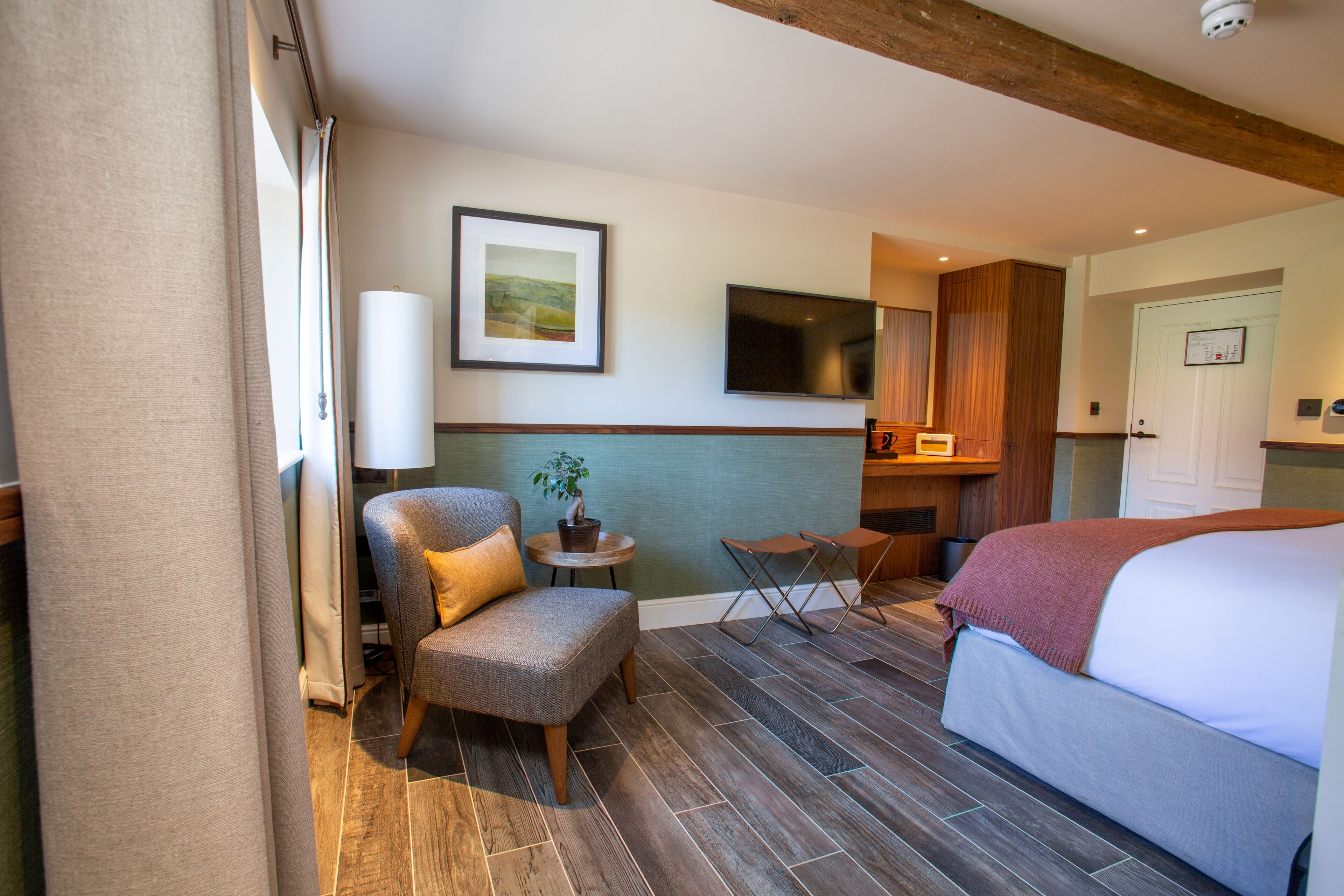 A hotel room with a bed, a chair, a small table, a TV, and a door.