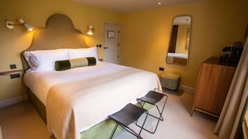A hotel room with a bed, bedside lamps, a mirror, a wooden dresser, and a small stool.