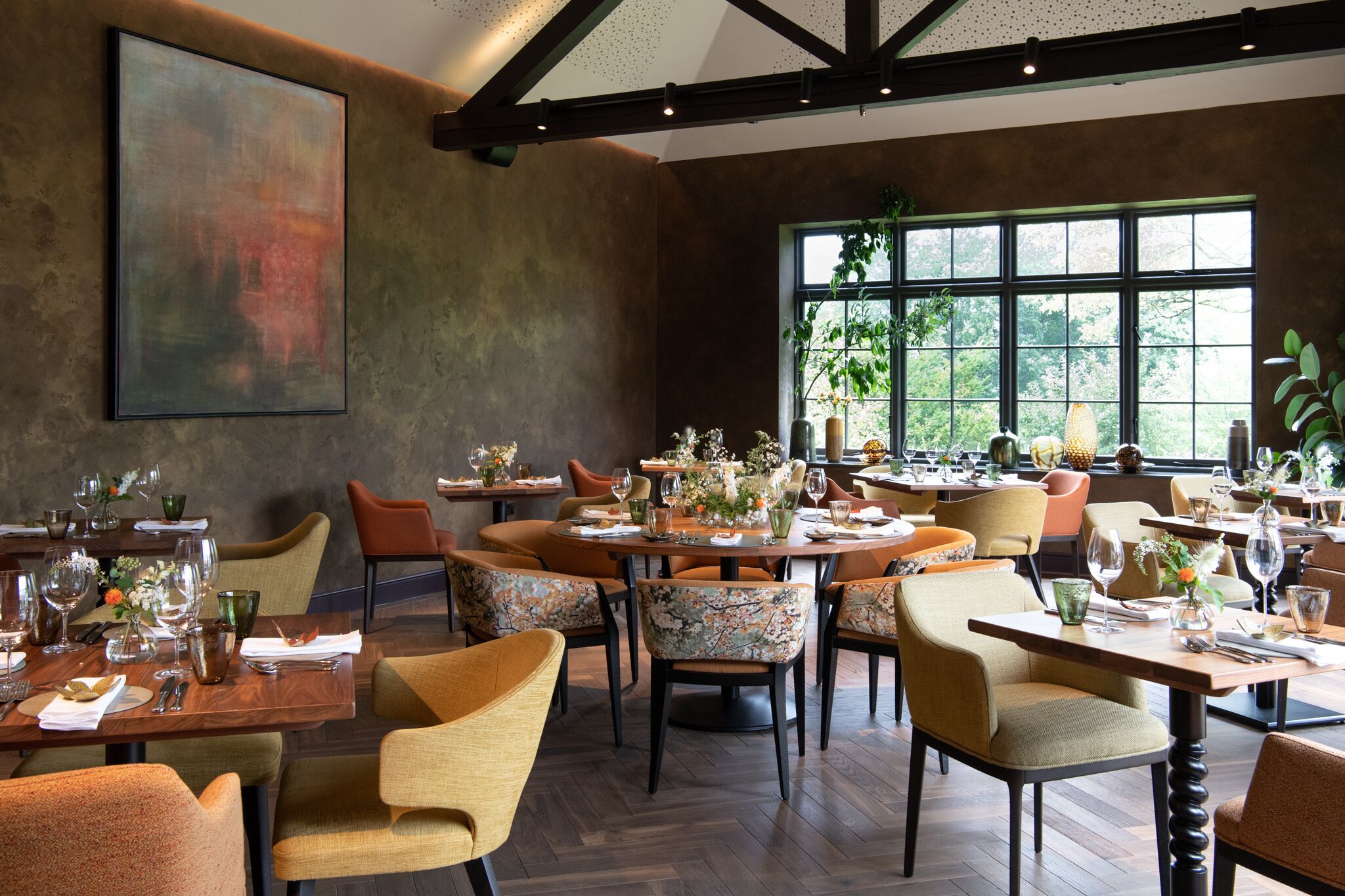 A restaurant with round tables, floral centerpieces, and a large window with a view of greenery.