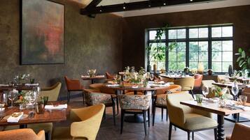A restaurant with round tables, floral centerpieces, and a large window with a view of greenery.