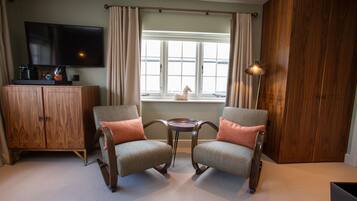 Quarto com duas poltronas, televisão, um armário de madeira e janela com cortinas.