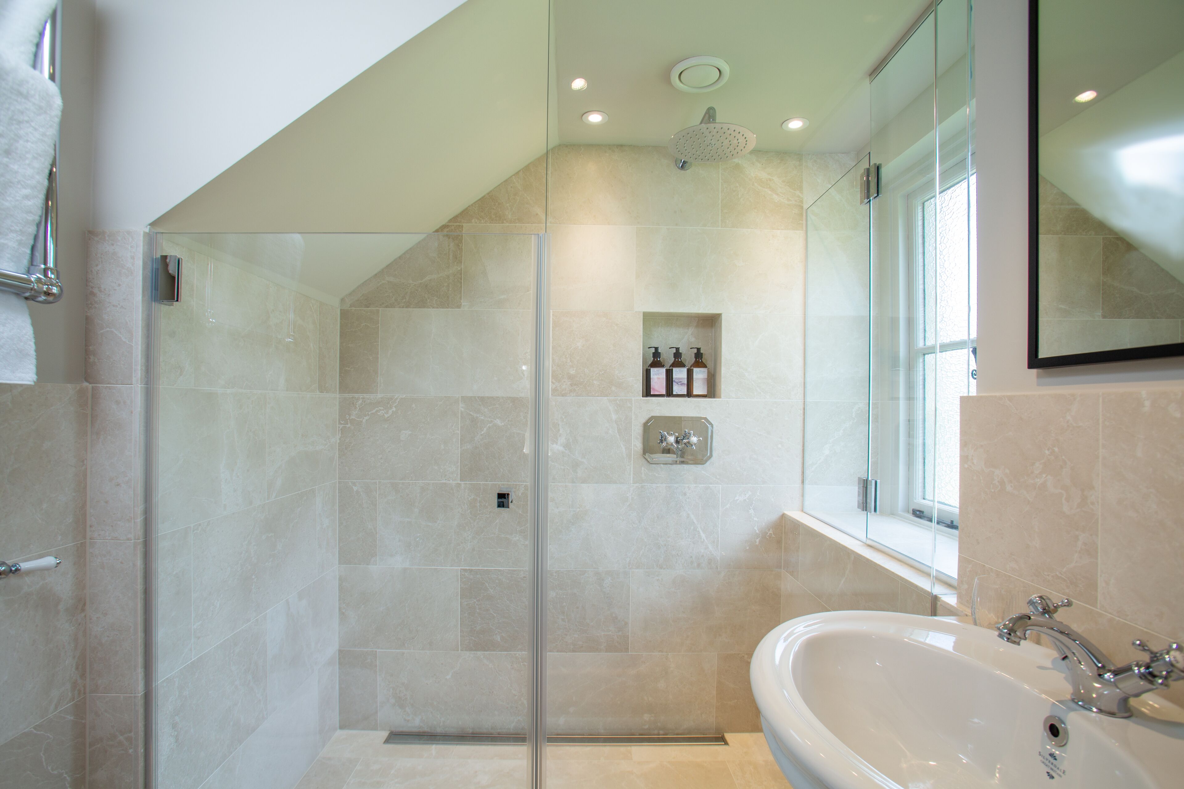 Ein modernes Badezimmer mit einer gläsernen Duschkabine, einer großen Badewanne und einem Fenster mit Tageslicht.