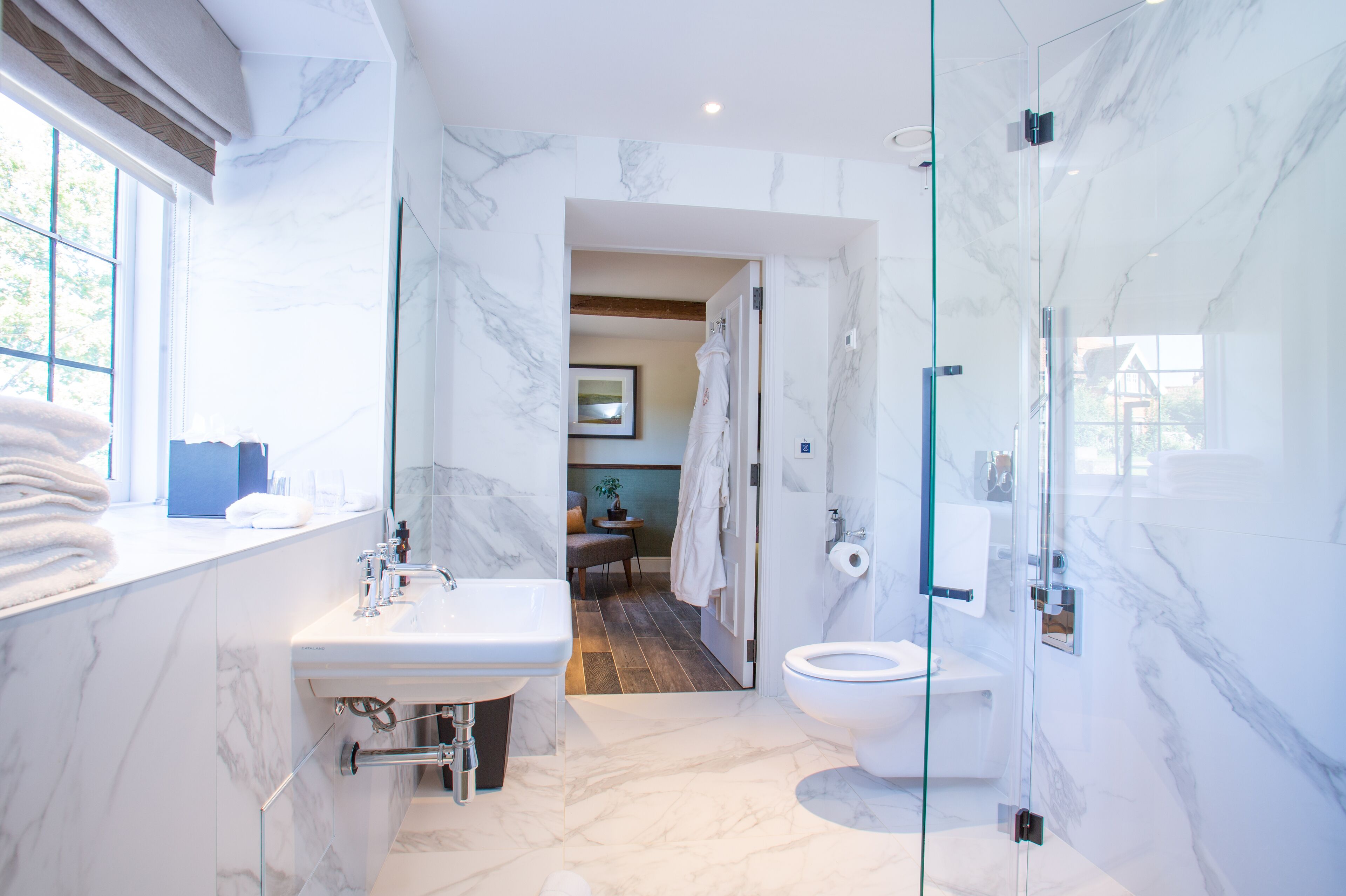 Un baño moderno con lavamanos de mármol, cabina de ducha de vidrio y vistas a una sala de estar.