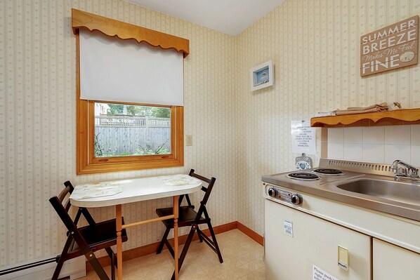 Una pequeña cocina con ventana, una mesa, dos sillas, estufa y lavabo.
