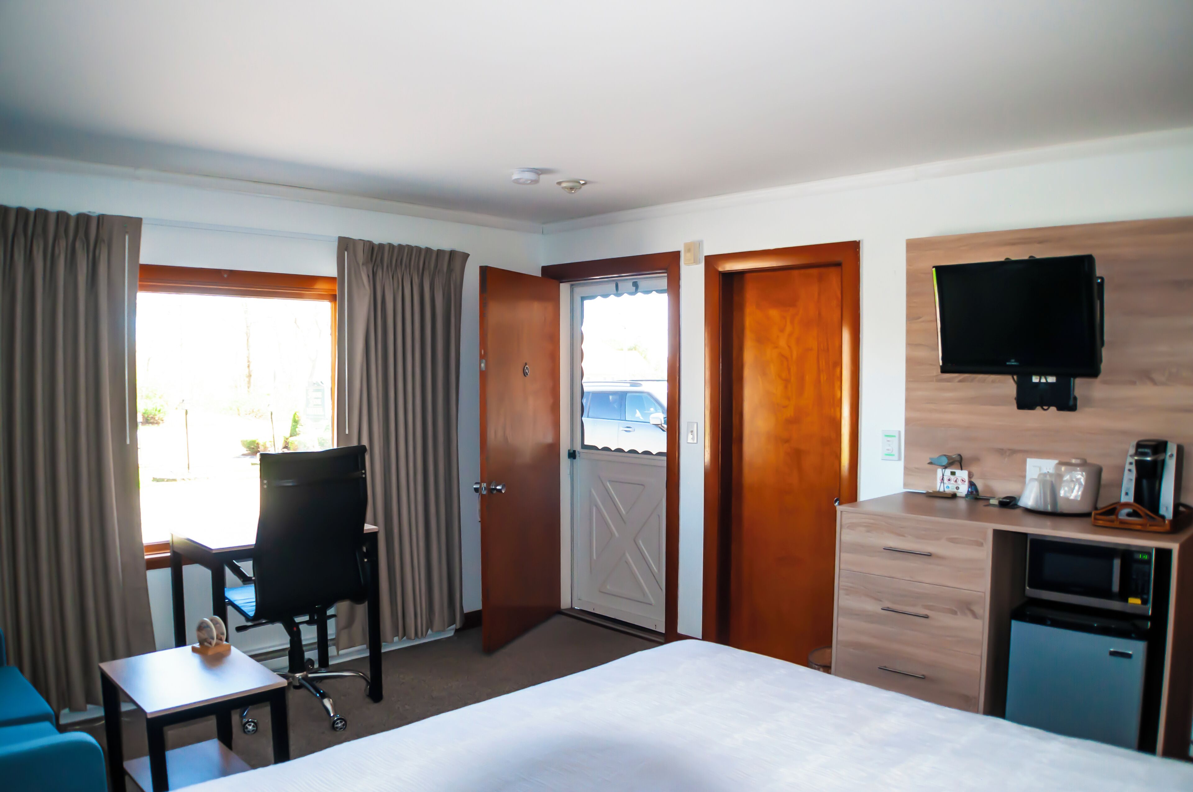 Una habitación de hotel con cama, escritorio, silla, televisor y kitchenette.