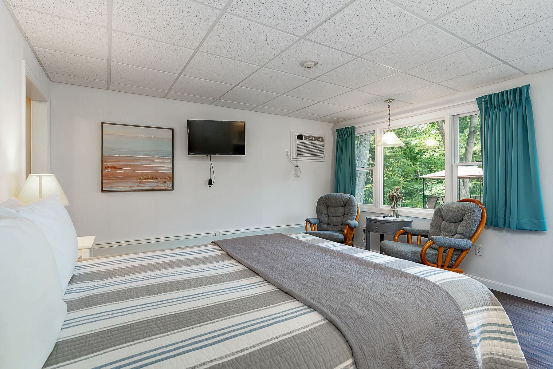 A hotel room with a large bed, two armchairs, a TV, and a window with curtains.