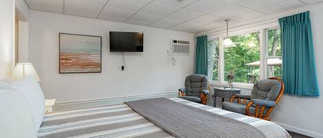 A hotel room with a large bed, two armchairs, a TV, and a window with curtains.