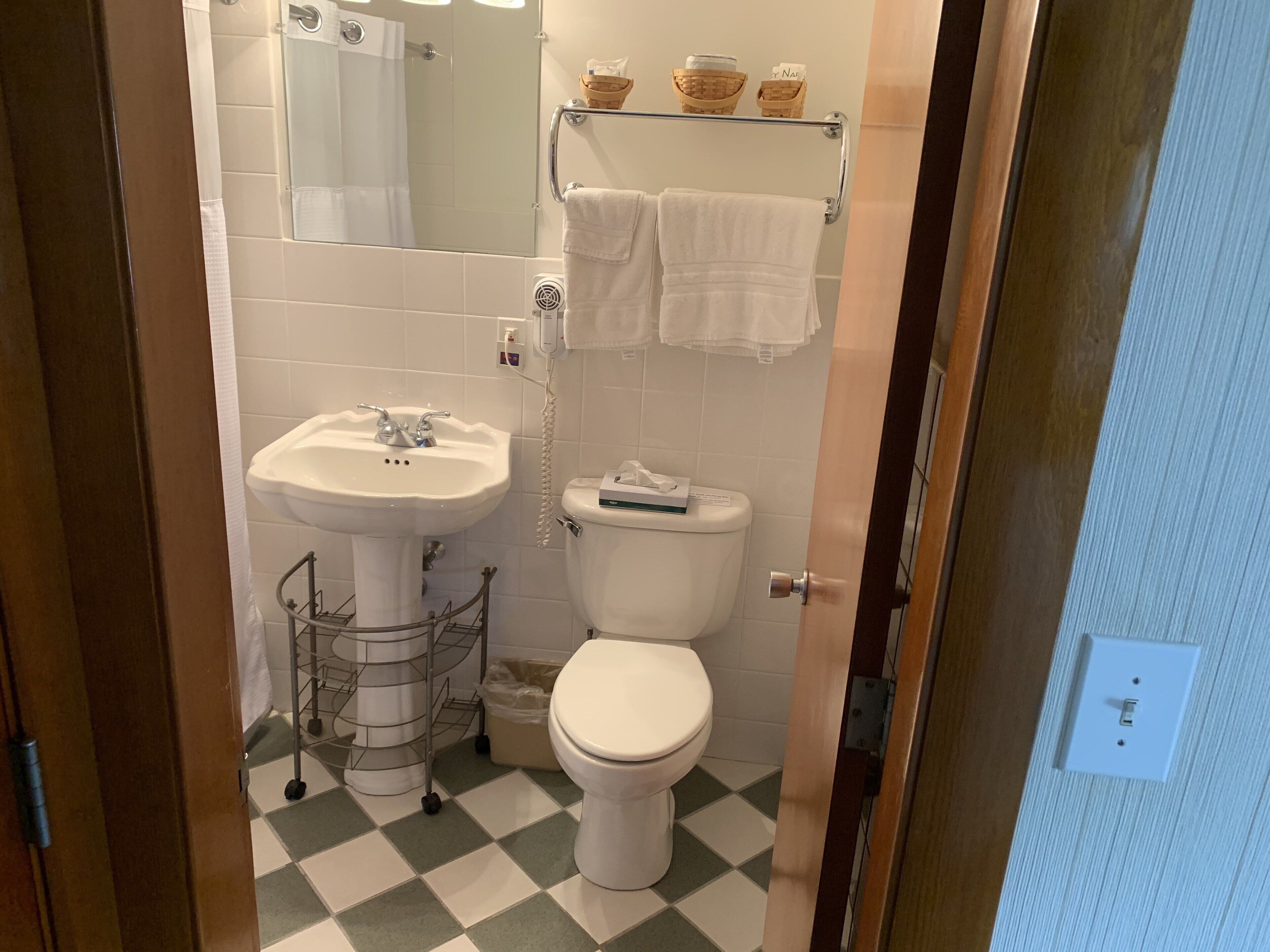 A bathroom with a sink, toilet, and a mirror. There are baskets on a shelf above the toilet.
