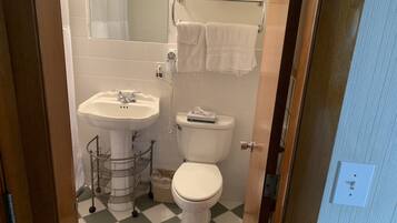 A bathroom with a sink, toilet, and a mirror. There are baskets on a shelf above the toilet.