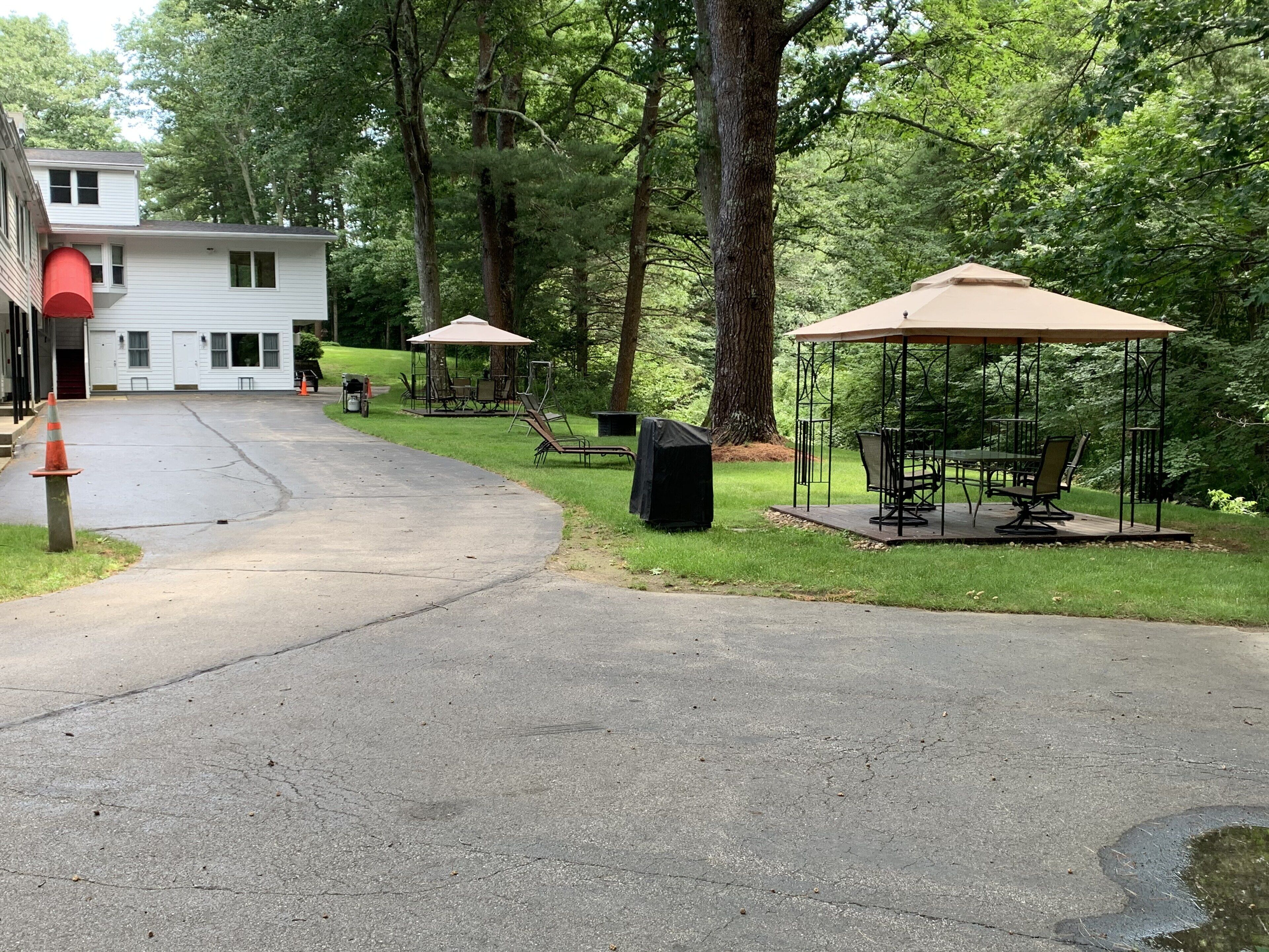 A paved driveway leading to a building with outdoor seating areas and a covered gazebo.