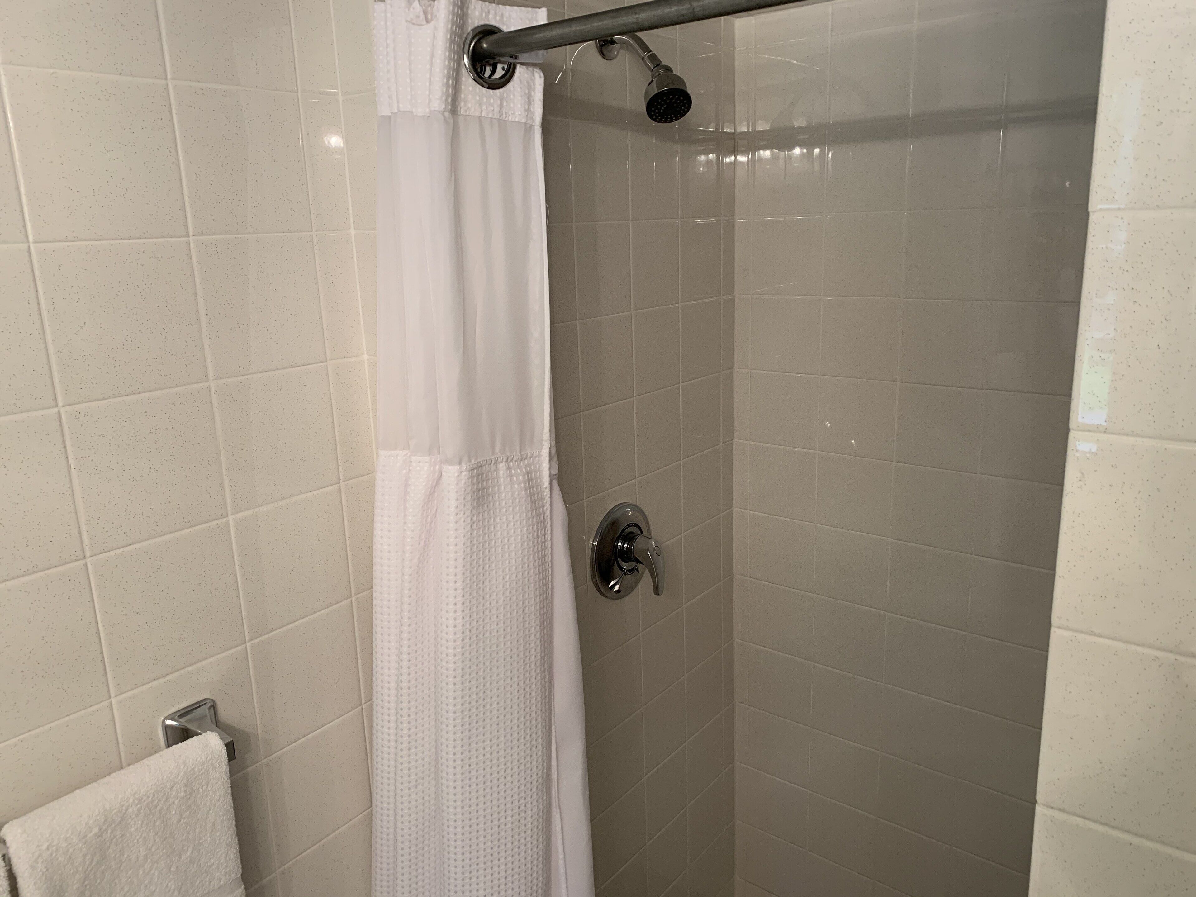 Une douche avec un rideau blanc, un pommeau de douche à main et un porte-serviettes avec une serviette blanche.