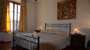 A bedroom with a bed, two bedside lamps, a window with curtains, a radiator, and a painting on the wall. - Appartamento Ilaria (San Macario in Monte/Lucca)