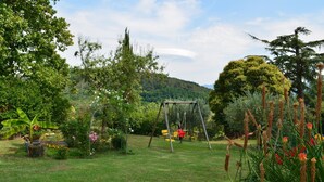 A garden with a swing set, various plants, and a mountainous backdrop. - Appartamento Ilaria (San Macario in Monte/Lucca)