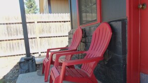 Two red Adirondack chairs outside a building with a stone wall and a wooden fence in the background. - The Gold Pan Motel (Eagle Nest)