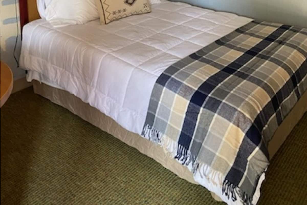 Une chambre d’hôtel avec un lit, un ventilateur de plafond, une lampe fixée au mur et une fenêtre.