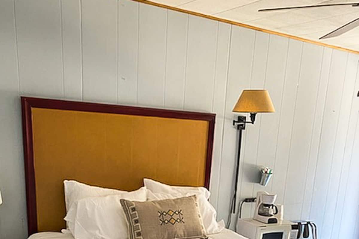 Un lit bien fait, recouvert d’une couverture à carreaux, avec une tête de lit en bois et une lampe de chevet.
