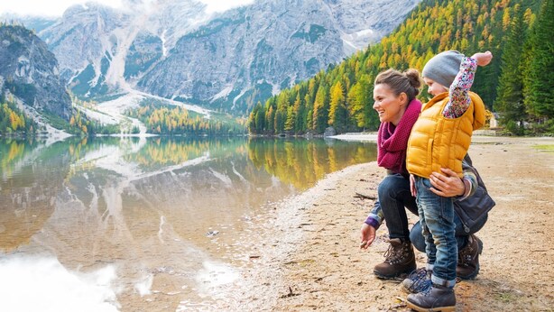 A lake with mountains in the background, a sandy shore, and two people sitting by the water's edge. - The Gold Pan Motel (Eagle Nest)