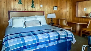 A hotel room with a wooden paneled wall, a bed with a blue plaid bedspread, two chairs, a small table, and a ceiling fan. - The Gold Pan Motel (Eagle Nest)
