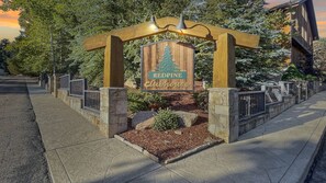 A wooden sign with 'REDPINE Clubhouse' written on it, supported by a wooden arch and stone pillars, with a landscaped area in front.