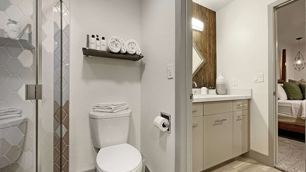 A bathroom with a toilet, a shower, and a sink with toiletries.
