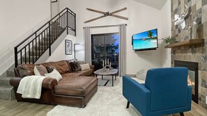 A living room with a brown leather sofa, a blue armchair, a fireplace, a television, and a staircase.