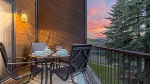 An outdoor dining area with a table set for four, chairs, and a view of a tree and landscape.