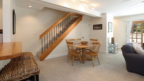 Un coin repas avec un escalier en bois, une table ronde entourée de chaises et une petite table d’appoint.