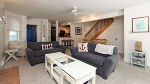 Un salon avec deux canapés, une table basse, un téléviseur et un escalier menant à la cuisine.