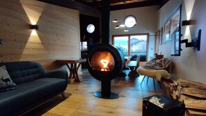 A cozy living room with a wood-burning stove, a sofa, a dining table, and a view of the outside. - GUEST CHALET WHITE FANG / CROC BLANC CHALET RELAXING 4 SAISONS (Morzine)