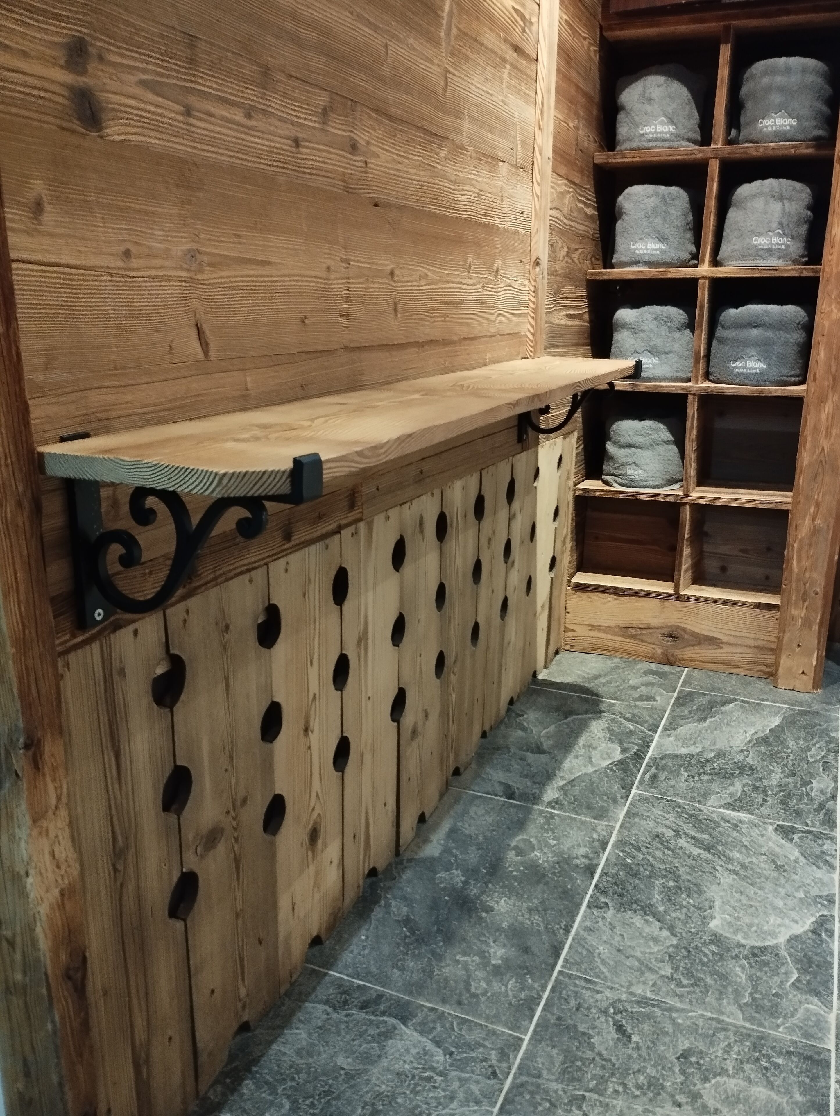 A wooden counter with a shelf, a wooden wall with circular cutouts, and a tiled floor.
