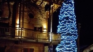 A wooden building with a balcony, a large Christmas tree with lights, and snow on the ground. - GUEST CHALET WHITE FANG / CROC BLANC CHALET RELAXING 4 SAISONS (Morzine)