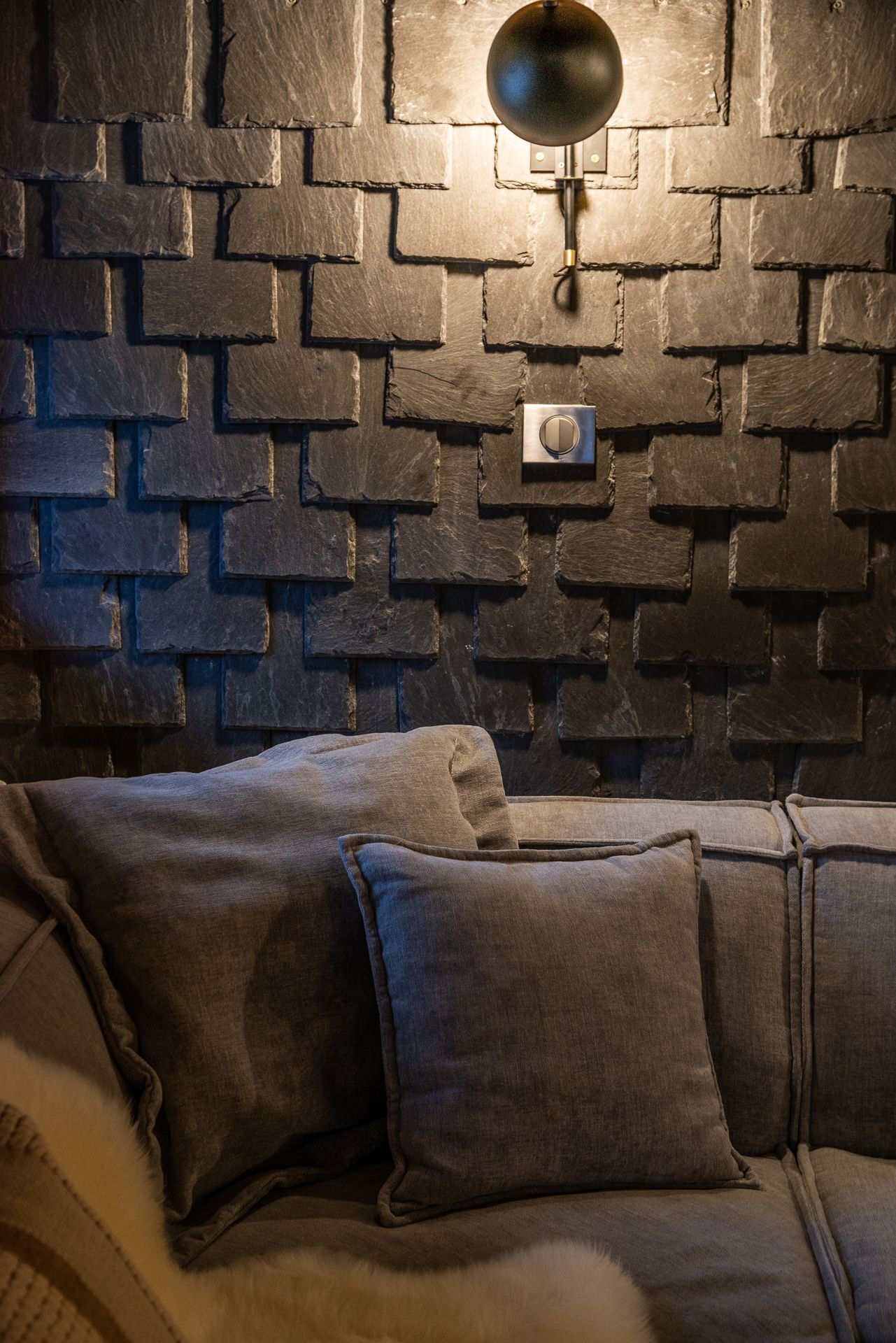 Un salon moderne avec un mur en pierre et un luminaire noir fixé au mur.